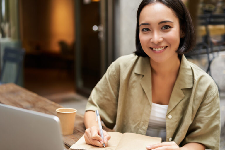 Portrait of young asian woman working on laptop, making notes, writing down while attending online lesson, work meeting