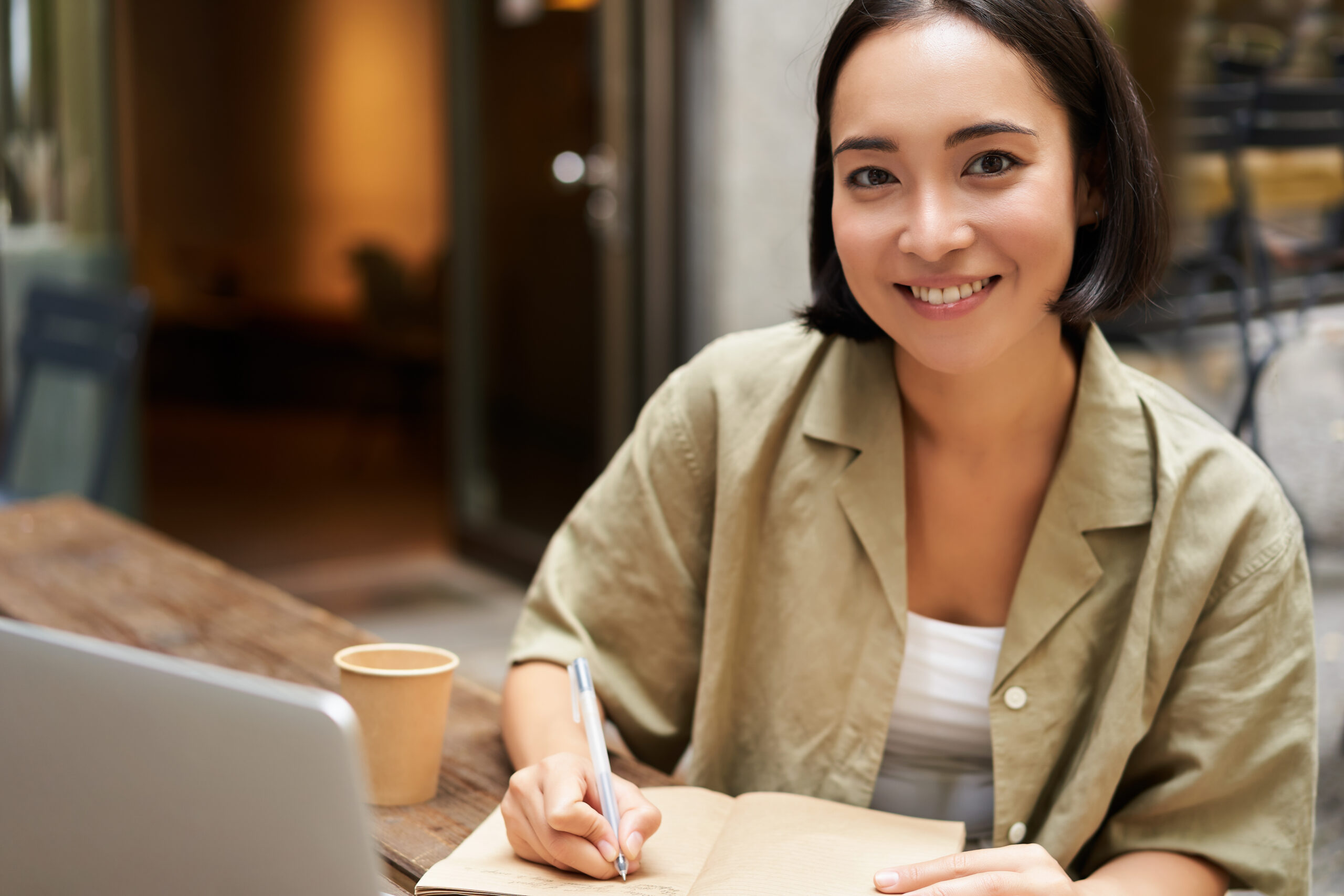 Portrait of young asian woman working on laptop, making notes, writing down while attending online lesson, work meeting