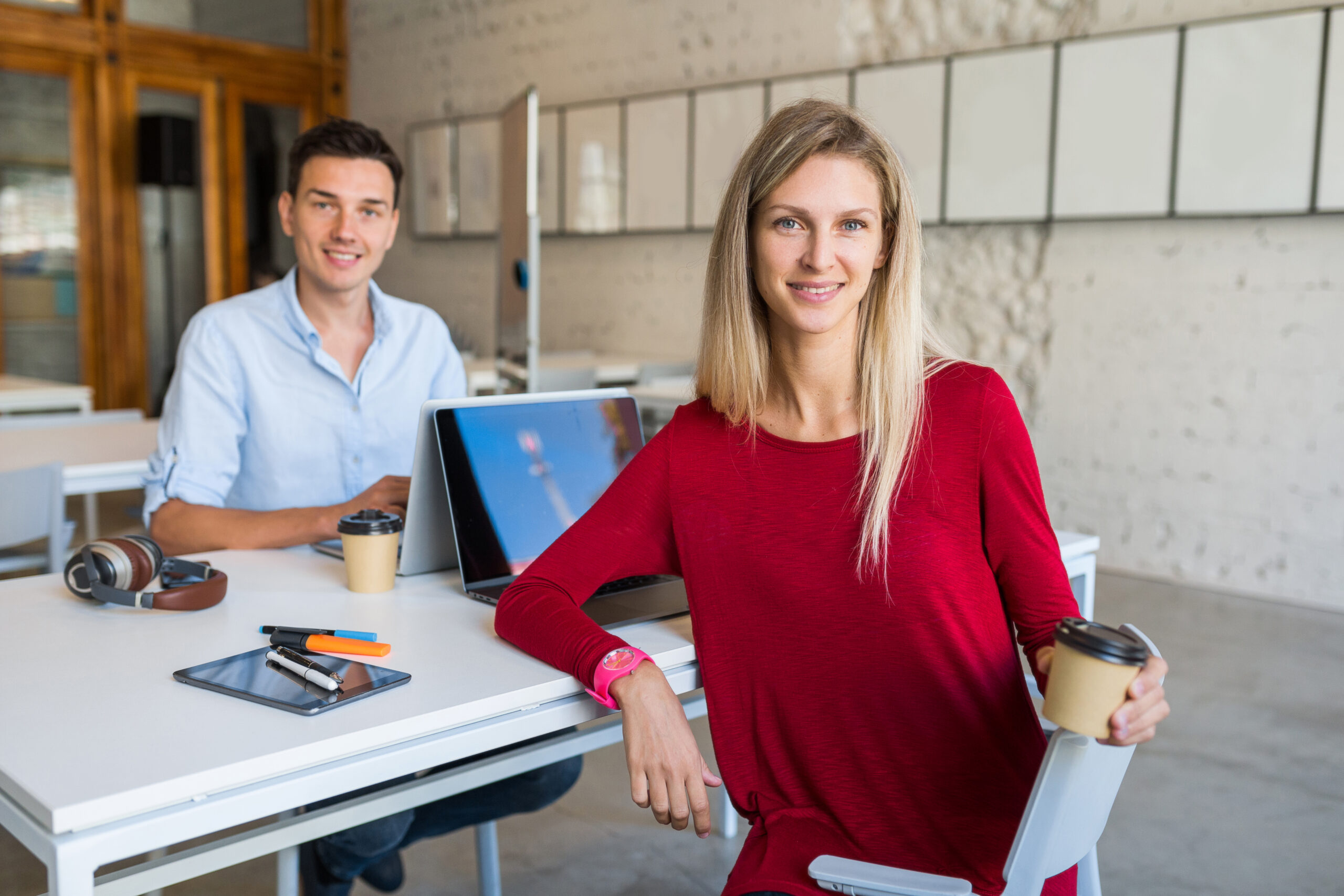 modern young people sitting at table, working at laptop in co-working office, attractive woman drinking cofee, thinking, startup team, freelancers, modern office room, open space, workplace